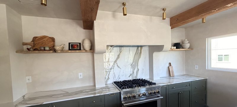 Range wall with a full-height Calacatta Gold marble slab backsplash, sage cabinets and oak shelves