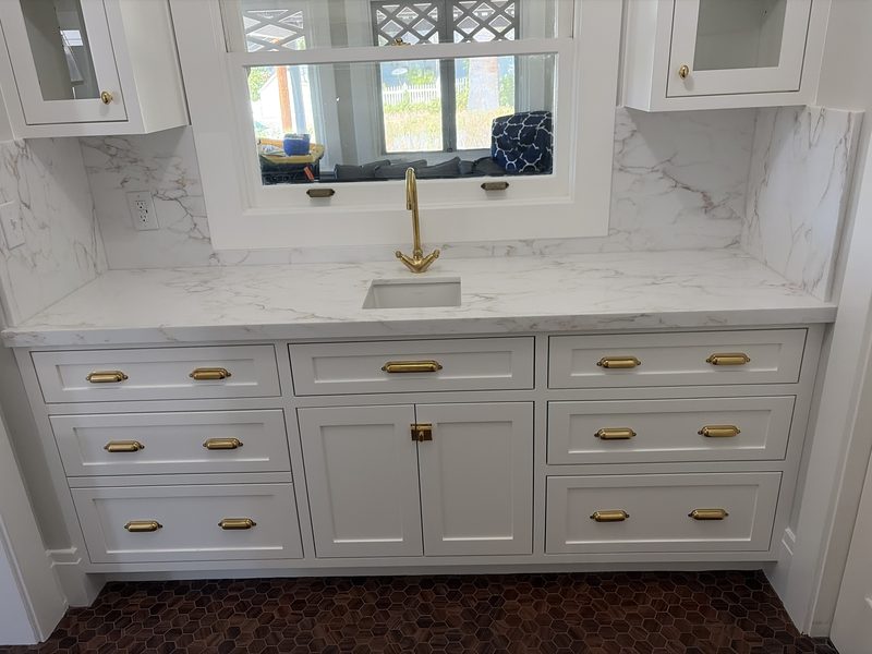 White cabinets with brass pulls, white quartz counter and backsplash around a pass-through window