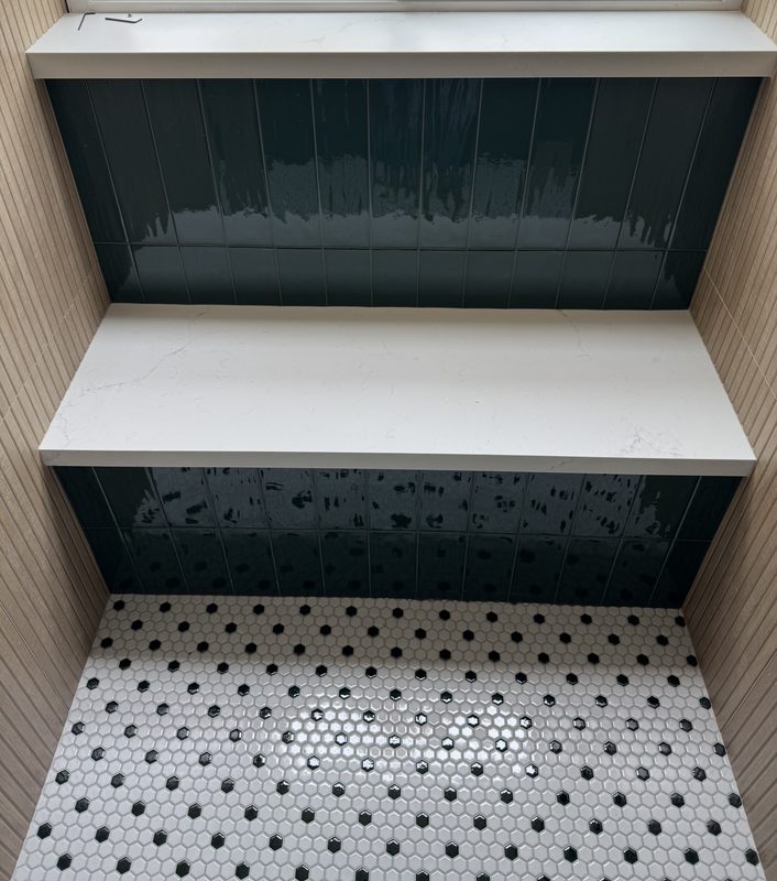 Shower with a white quartz bench and ledge, dark glazed tile and black-and-white hex floor