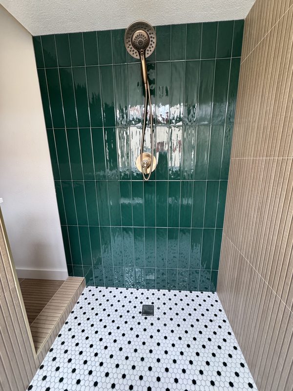 Walk-in shower with deep green glazed vertical tile, brass shower head and black-and-white hex floor