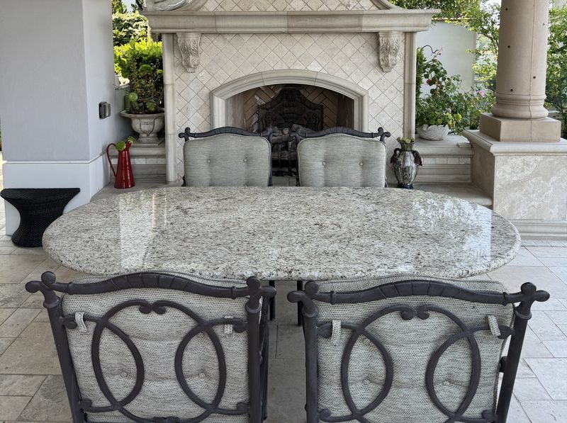 Oval granite patio table with a rounded full bullnose edge, in front of an outdoor stone fireplace
